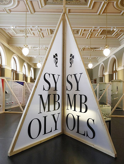  VÝSTAVA SYMBOLY V HISTORICKÉ BUDOVĚ NÁRODNÍHO MUZEA / Výstava se zabývá státními symboly České republiky a ukazuje jejich vznik a proměnu od roku 1918 až do současnosti. Výtvarné zpracování výstavy vychází z trojúhelníkové výseče ve vlajce, se kterou se volně pracuje jako s prostorovým a konstrukčním prvkem expozičních stěn. Základním stavební materiálem jsou dřevěné hranoly, které jsou vyplněny mléčným polykarbonátem.