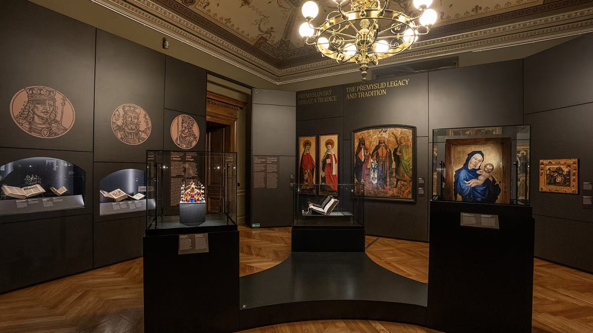  PŘEMYSLOVCI / NÁRODNÍ MUEZUM/ Výstava Přemyslovci v Národním muzeu představuje  dynastii jako mnohovrstevnatý fenomén – síť vztahů,  moci, víry a identity, která přetváří kulturní i fyzický  prostor. Architektonický koncept výstavy se opírá o tři  základní atributy dynastie: KORUNA, KŘÍŽ, KRUH –  symboly vlády, víry a rodiny. Tyto prvky se promítají  jak do kurátorského narativu, tak do výtvarného  a materiálového řešení výstavního prostoru. 